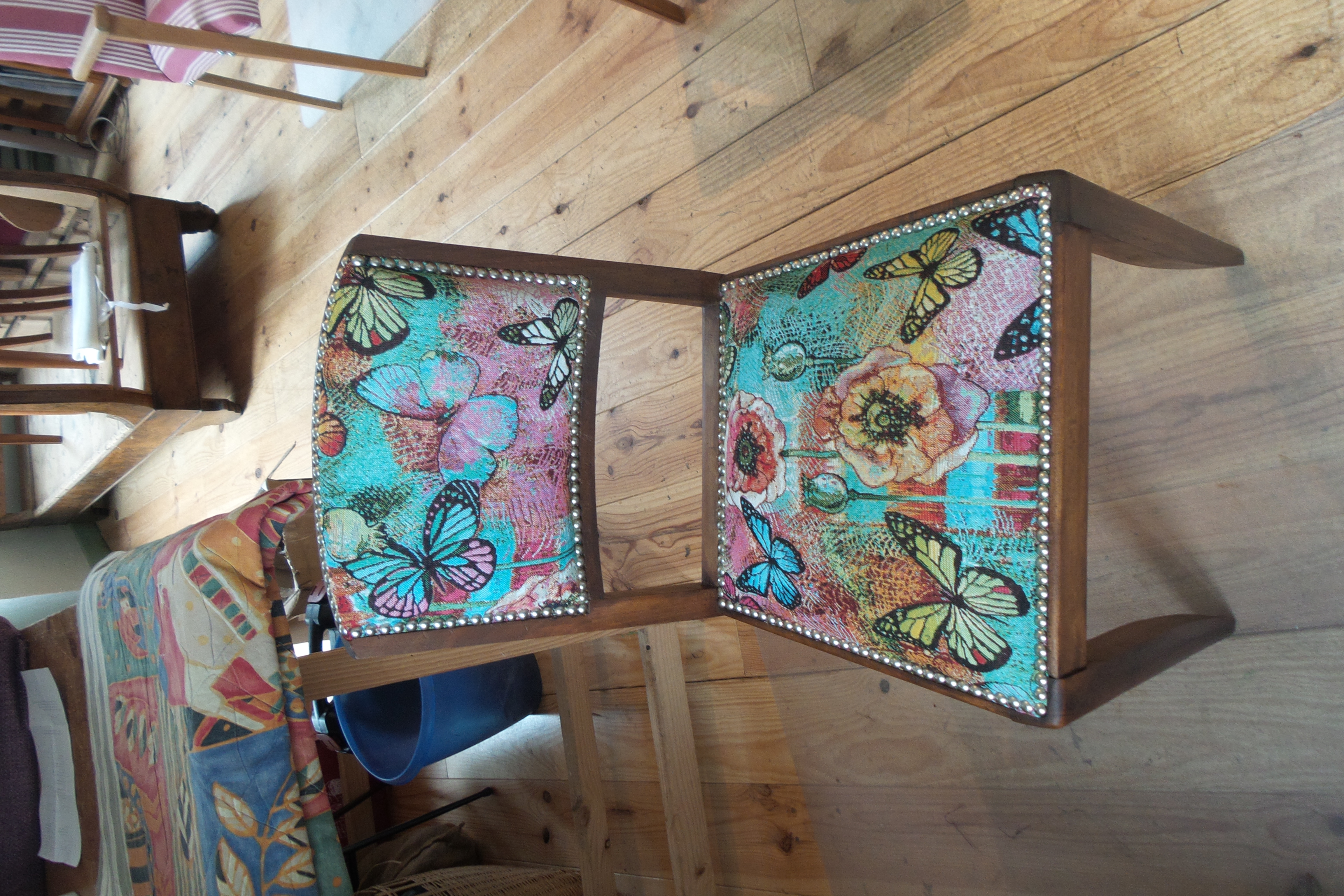 Petite chaise recouverte d'un tissu coloré à motifs de papillons
            et de fleurs. Finition : clous nickel mat